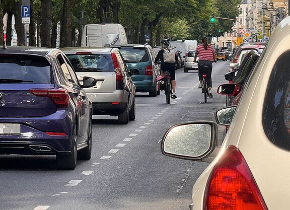 Zwei Radfahrende fahren auf einem schmalen Schutzstreifen neben parkenden Autos auf der Oppenhoffallee in Aachen. Der geringe Abstand zu parkenden Fahrzeugen verdeutlicht die problematische Verkehrsführung. Oppenhoffallee: Heutige Situation