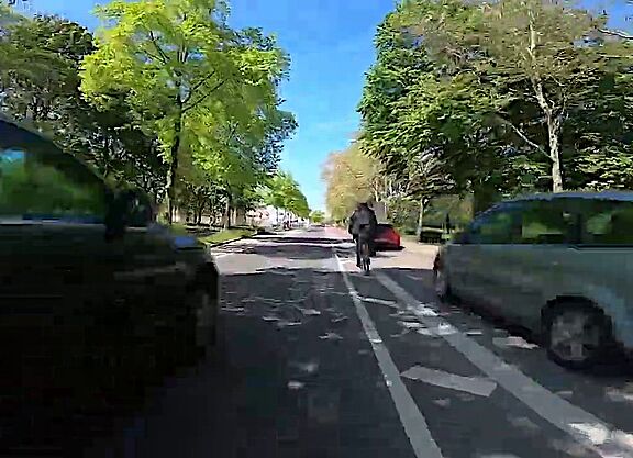 Stellungnahme von ADFC/ProRad Düren zur Veldener Straße Ein Fahrradfahrer fährt neben einem zugeparkten Radstreifen, während sich ein weiteres Kfz von hinten nähert