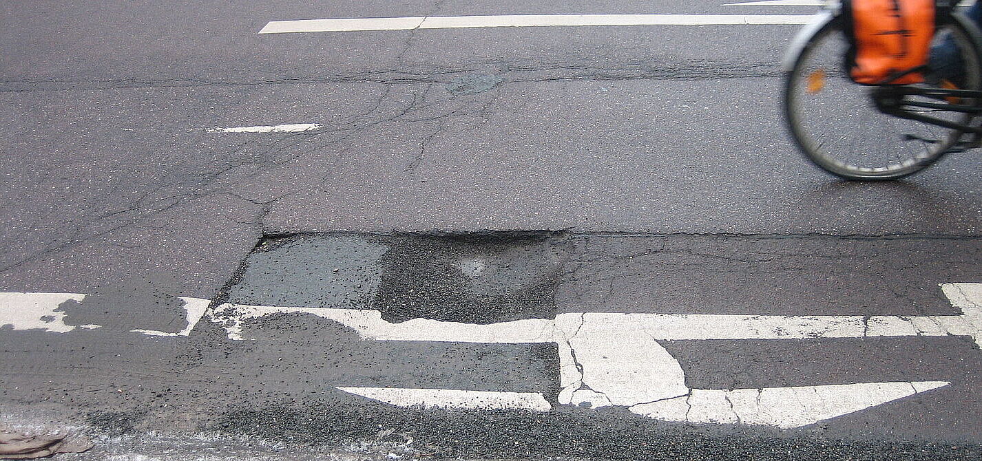Schlagloch auf der Straße Ein Schlagloch auf der Straße, man sieht noch das Hinterrad eines vorbeifahrenden Fahrrads.